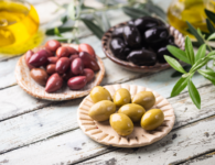 Green, red and black Musco olives sitting on a table in bowls with olive oil