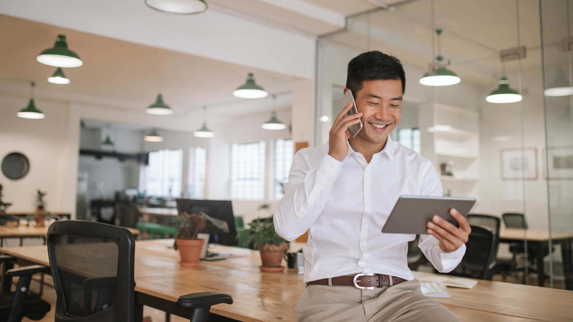 Satisfied employee smiles while talking on the phone and viewing a tablet