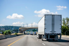 Rear-view of a white big rig going down the highway about to pass under a bridge